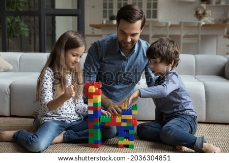 Happy best dad and two sibling children playing together on warm floor, building toy tower on clean carpet, constructing model from plastic blocks, improving creativity in game. Family home activity Royalty-Free Stock Photo #2036304851