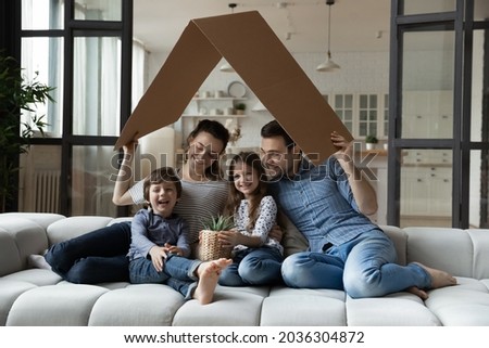 Happy sibling kids and parents holding carton toy roof above heads, showing symbol of home, safety, celebrating buying new house, property, health insurance. Real estate, mortgage, family concept Royalty-Free Stock Photo #2036304872