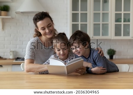 Happy mom and two children enjoying book story in kitchen. Mother entertaining kids at home, teaching boy and girl to read, improving imagination, interest to literature. Family smart activity Royalty-Free Stock Photo #2036304965