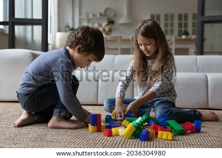 Cute sibling kids constructing toy tower, completing model form heap of blocks. Focused boy and girl sitting on carpet on heating floor at home, playing learning game, training skills Royalty-Free Stock Photo #2036304980