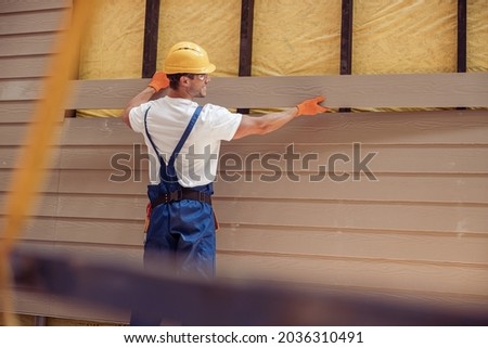 Smiling male worker building cabin at construction site Royalty-Free Stock Photo #2036310491