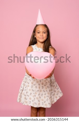 adorable happy smiling little child girl in birthday hat celebrating with pastel pink air balloon on pink background. birthday party.