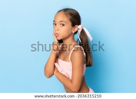 Keep Silence Concept. Cheerful child putting finger on lips, copy space, pastel blue studio wall