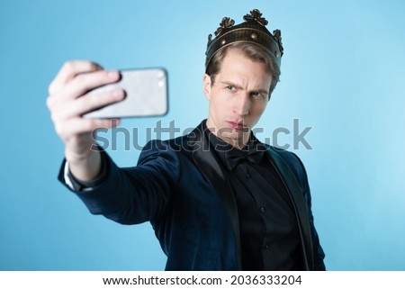 Brag about your success on social networks. A young man has received an achievement and takes a selfie. A guy in a suit with a crown on his head Royalty-Free Stock Photo #2036333204