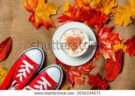 Romantic cup of coffee and gumshoes with autumn leaves on burlap background. Top view