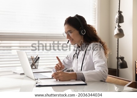 Happy attentive general practitioner in headset using laptop, giving online help, medical support, advice, consultation, talking to patients, making video conference call. Telehealth concept Royalty-Free Stock Photo #2036344034