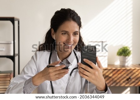 Happy focused female doctor in earphones using mobile phone for video call, talking to patient, giving medical consultation, healthcare advice, explaining treatment. Telemedicine, remote counseling Royalty-Free Stock Photo #2036344049