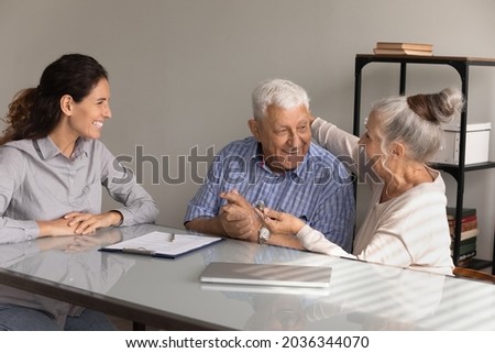Happy elderly husband and wife holding key, hugging and laughing at realtor office. Smiling laughing real estate agent feeling joy for senior couple of clients excited with house buying