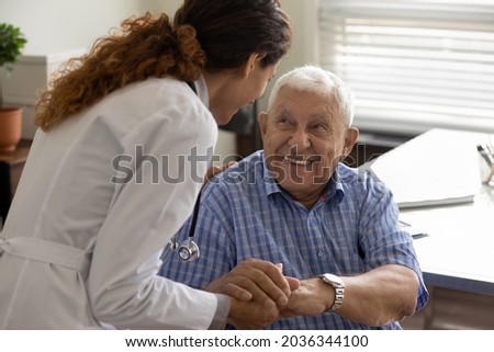 Friendly young female doctor and optimistic elder 80s man meeting in office for consultation. GP therapist holding hands of old patient, giving sympathy, support, advice about treatment Royalty-Free Stock Photo #2036344100