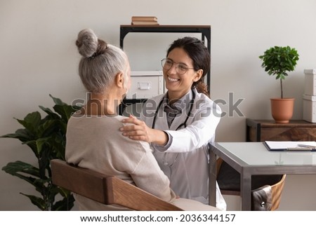Happy satisfied GP doctor telling good news to elder patient, congratulating on optimistic medical checkup result, giving support, empathy, touching shoulder of senior woman at appointment in office Royalty-Free Stock Photo #2036344157