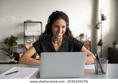 Happy millennial business woman in headset, working at laptop from home, making video call, talking to coworkers online on virtual conference meeting. Support manager speaking to client, smiling