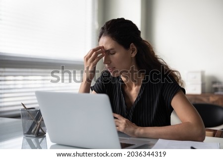 Sad frustrated millennial woman tired of work at computer, feeling unwell, suffering from stress, headache, dry irritable eyes. Businesswoman touching head at workplace. Fatigue, burnout concept Royalty-Free Stock Photo #2036344319