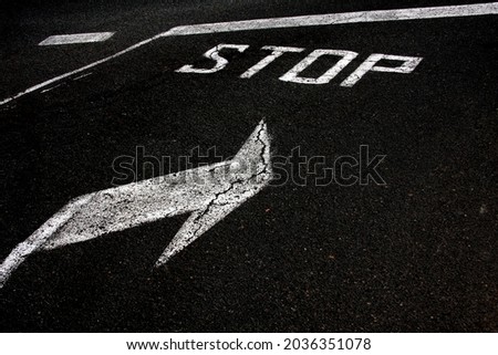 bright white road sign uppercase capital letter STOP and direction arrows on new textured black asphalt 