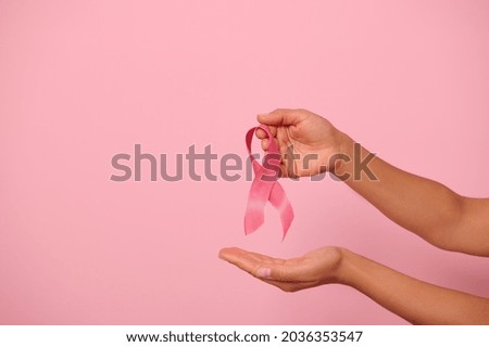 Close-up of woman's hands holding a pink ribbon, symbol of World Breast Cancer awareness Day, 1 st October. Woman's health and medical concept, national Cancer Survivor Day, isolated with copy space