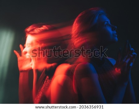 Dual personality. Bipolar mind. Mood disorder. Mental health. Split identity. Woman with depressed peaceful emotion in bright red blue neon light color isolated on dark background. Royalty-Free Stock Photo #2036356931