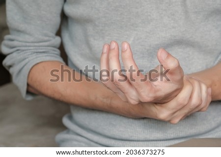 Asian man holding hand with muscle weakness, numbness and paralysis symptoms after vaccination. Guillain Barre syndrome rare cause by autoimmune disorder concept. Selective focus. Royalty-Free Stock Photo #2036373275
