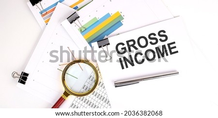 GROSS INCOME text on white paper on light background with charts paper
