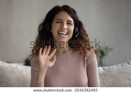 Joyful beautiful millennial hispanic woman in headset with microphone looking at camera, waving hand starting online video call conversation, passing job interview distantly or communicating remotely. Royalty-Free Stock Photo #2036382485