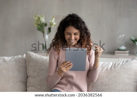 Overjoyed emotional young latina woman looking at digital tablet screen, celebrating online lottery auction betting giveaway win, feeling excited reading email with amazing news, internet success. Royalty-Free Stock Photo #2036382566