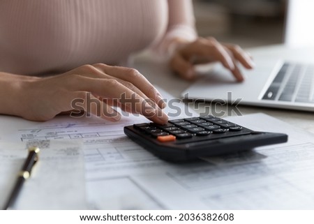 Close up young woman using calculator, summarizing utility bills, managing household budget, planning domestic savings or investments, financial accounting using e-banking application concept. Royalty-Free Stock Photo #2036382608
