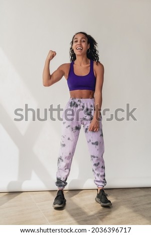 attractive black african american woman in stylish hipster fitness outfit violet top and pants on white isolated background, summer fashion trend, strong muscles sport style