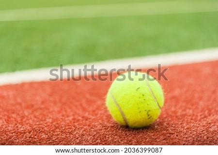 A yellow tennis ball is on the red tennis court.
