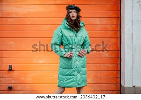 stylish woman posing in winter autumn fashion trend puffer coat and hat beret against orange wall in street Royalty-Free Stock Photo #2036402117
