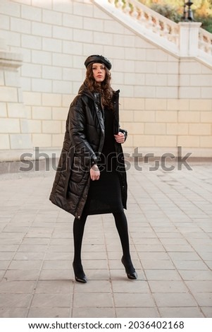 stylish woman posing in winter autumn fashion trend black puffer coat and leather hat beret in old beautiful street wearing high heel shoes Royalty-Free Stock Photo #2036402168