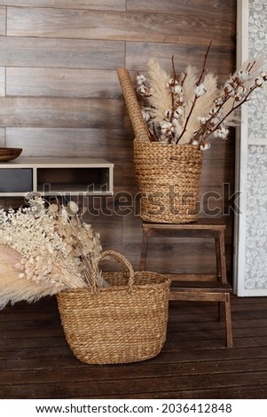  Living room hygge, cozy home decor. Scandinavian interior living room. Room in bohemian style. Rustic style. dry pampas grass and flowers. Wicker baskets with dried flowers near table on wooden floor