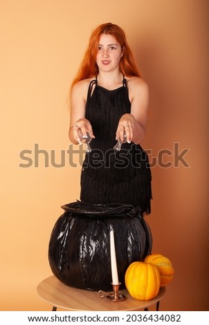red-haired girl witch on The holiday Halloween brews a potion in the cauldron next to pumpkins and a spider