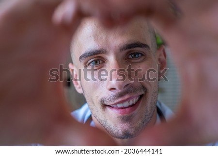 Close up portrait of smiling young caucasian male nurse or GP in white medical uniform show heart love hand gesture. Happy young man doctor show support and care to patients or client in hospital.