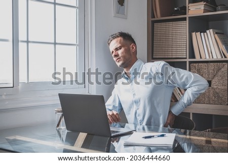 Close up rear view stressed young man touching lower back feeling discomfort, suffering from sudden pain due to sedentary lifestyle or long computer overwork in incorrect posture at home office. Royalty-Free Stock Photo #2036444660