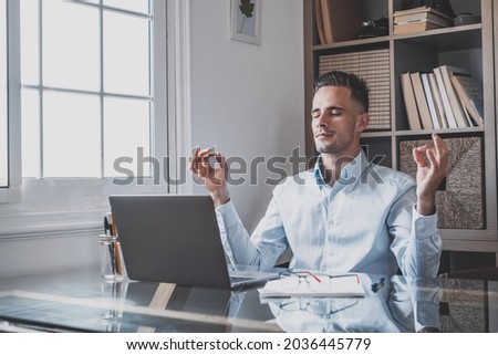 Serene office male teenager sit at desk relaxing doing yoga, practice meditation to reduce stress relief fatigue feel internal balance at workplace, improve mindfulness, maintain mental health concept Royalty-Free Stock Photo #2036445779
