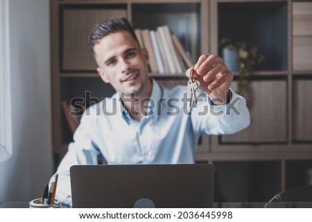 Focus on bunch of keys from house flat apartment in hand of smiling male. Blurred portrait of confident man professional realtor offering new dwelling real estate unit to potential buyer. Close up Royalty-Free Stock Photo #2036445998