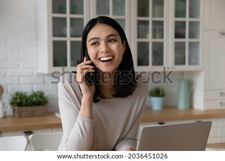 Happy beautiful young korean asian woman listening good news involved in pleasant phone call conversation, distracted from computer work, talking speaking with friends, distant communication concept. Royalty-Free Stock Photo #2036451026