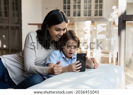 Affectionate surprised young asian korean mother and little cure kid son looking at cellphone screen, feeling excited of winning mobile game, getting promo code purchasing goods in internet store.