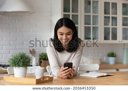 Smiling young asian vietnamese woman using mobile software applications, typing message communicating in social network, reading email with pleasant news, shopping in internet store or playing game. Royalty-Free Stock Photo #2036451050