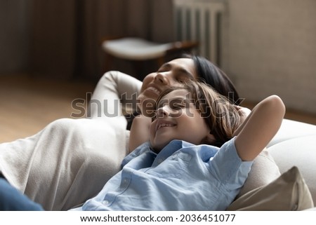 Happy young asian vietnamese mother daydreaming napping with smiling small child son on comfortable sofa, enjoying spending carefree mindful weekend time, breathing fresh air resting together at home. Royalty-Free Stock Photo #2036451077