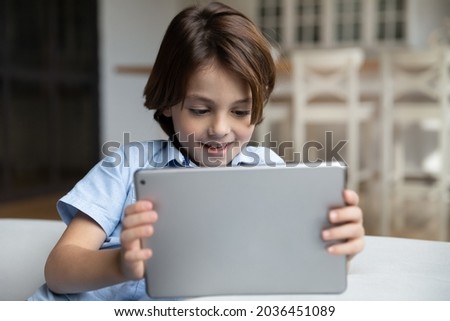 Happy small cute kid boy holding digital computer tablet, playing online games, using educational apps, communicating in social network, having fun online, internet security, modern tech addiction.