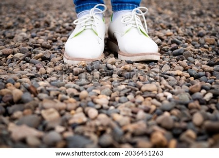 Women's feet in street shoes, standing on the stones. White sneakers and blue jeans.