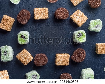 A multi-colored Turkish delight (rahat locum) with pistachio, milk and cocoa flavors creates a frame. Place for your text. Traditional oriental sweetness. Blue background. Flat lay. Copy space