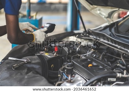 Expertise mechanic working in automobile repair garage. battery inspection. Black male mechanic car checking Battery Capacity Tester Voltmeter. Royalty-Free Stock Photo #2036461652