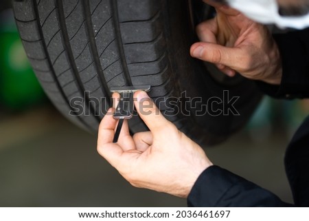 Mechanic checking checking the depth of car tire tread.  Car maintenance and auto service garage concept. Royalty-Free Stock Photo #2036461697