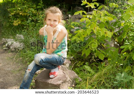 Young girl sitting on a rock thinking staring straight at the camera with her chin on her hand and a pensive expression