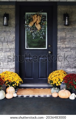 Front porch decorated for Thanksgiving Day with homemade wreath hanging on door. Heirloom gourds,  white, green and orange pumpkins, and colorful mums give an inviting atmosphere.