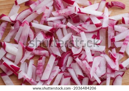 Finely chopped fresh radish strips on a wooden cutting board with a solid background Royalty-Free Stock Photo #2036484206