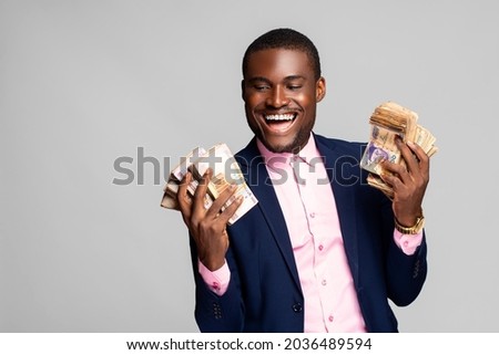 happy young african man holding a lot of money that he has won, feeling excited Royalty-Free Stock Photo #2036489594