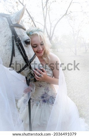 Portrait of beautiful fantasy woman and white horse wrapped in wedding veil with mist around them.