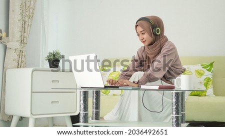 asian woman in hijab working from home typing laptop while listening