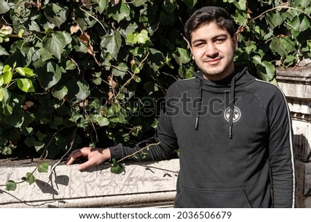 Attractive smiling young Latino man leaning on a concrete railing.
